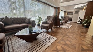 A spacious living area with a brown leather sofa, two armchairs, a glass coffee table, and a patterned rug. - Trademark Collection By Wyndham Operla İstanbul Airport Hotels (Arnavutköy)