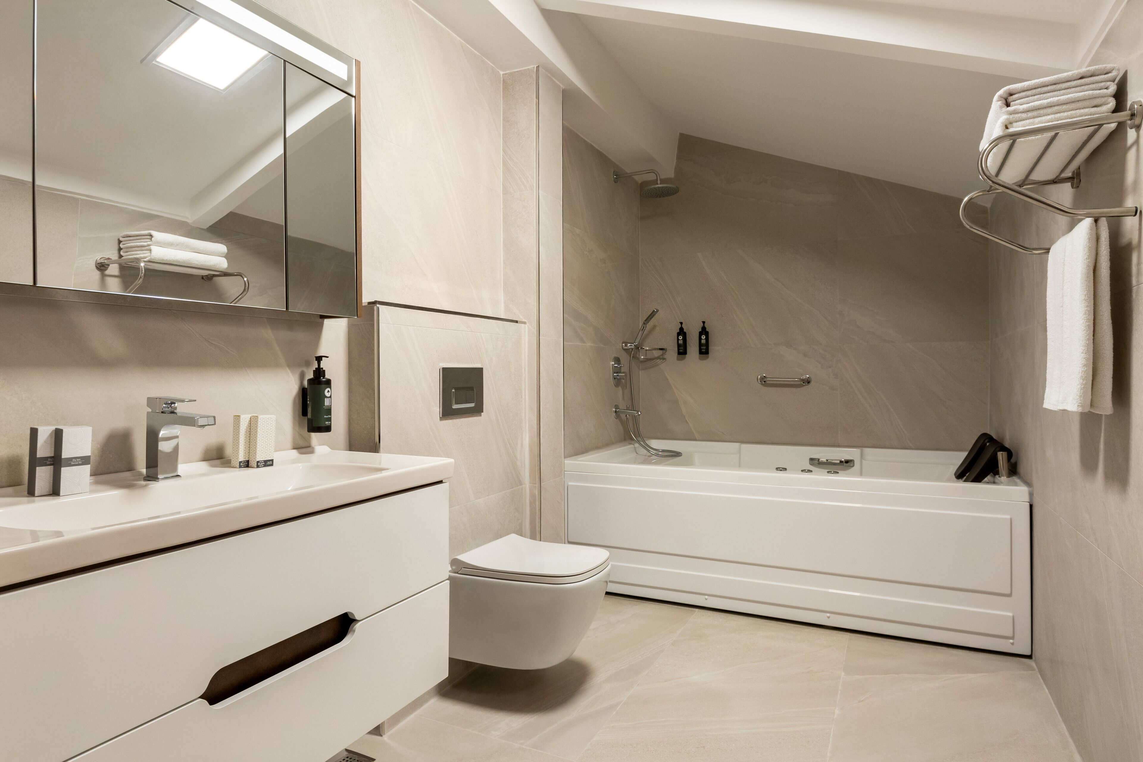 A modern bathroom with a large mirror, a sink, a toilet, and a bathtub.