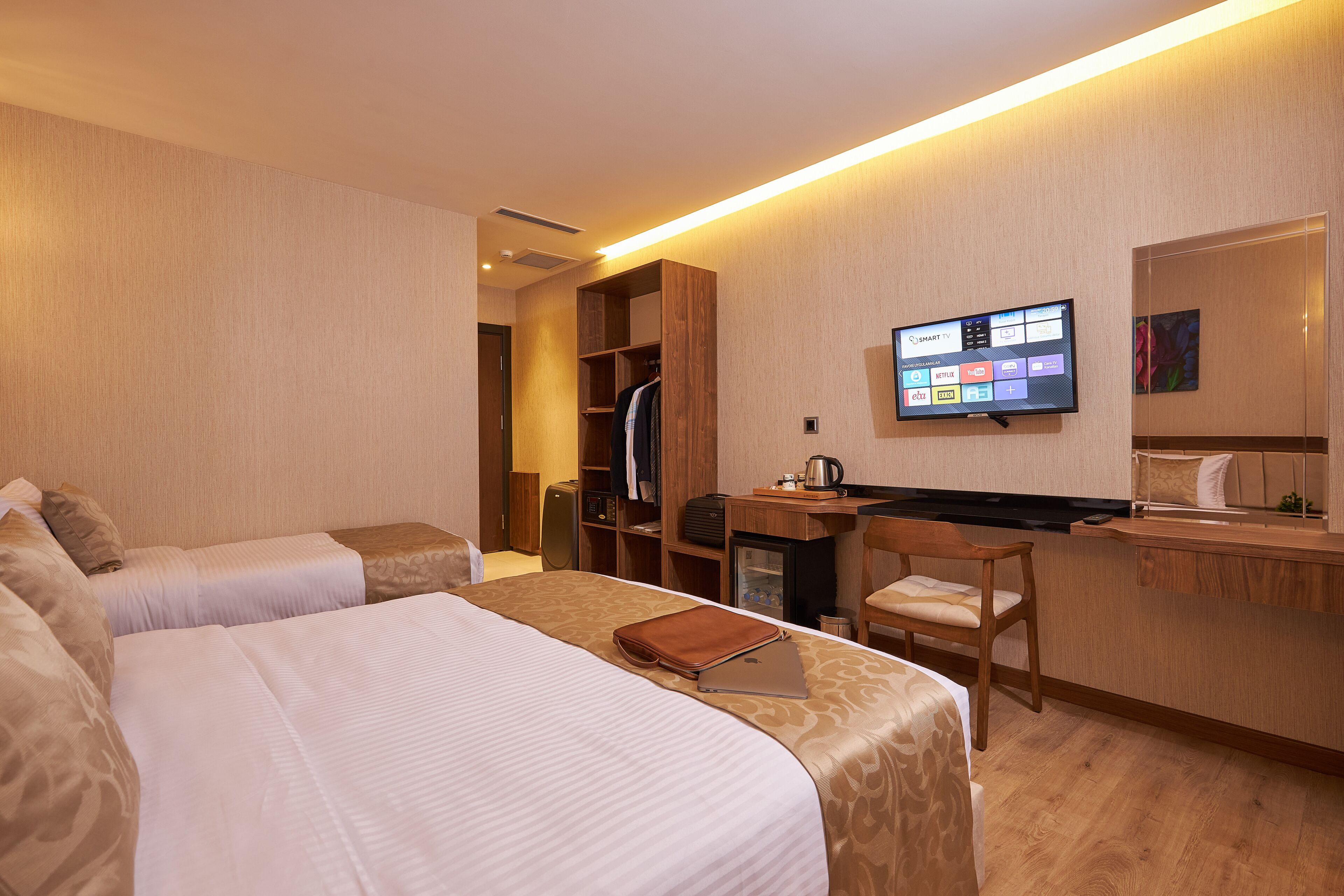 A hotel room with two beds, a desk, a chair, a television, and a kitchenette.