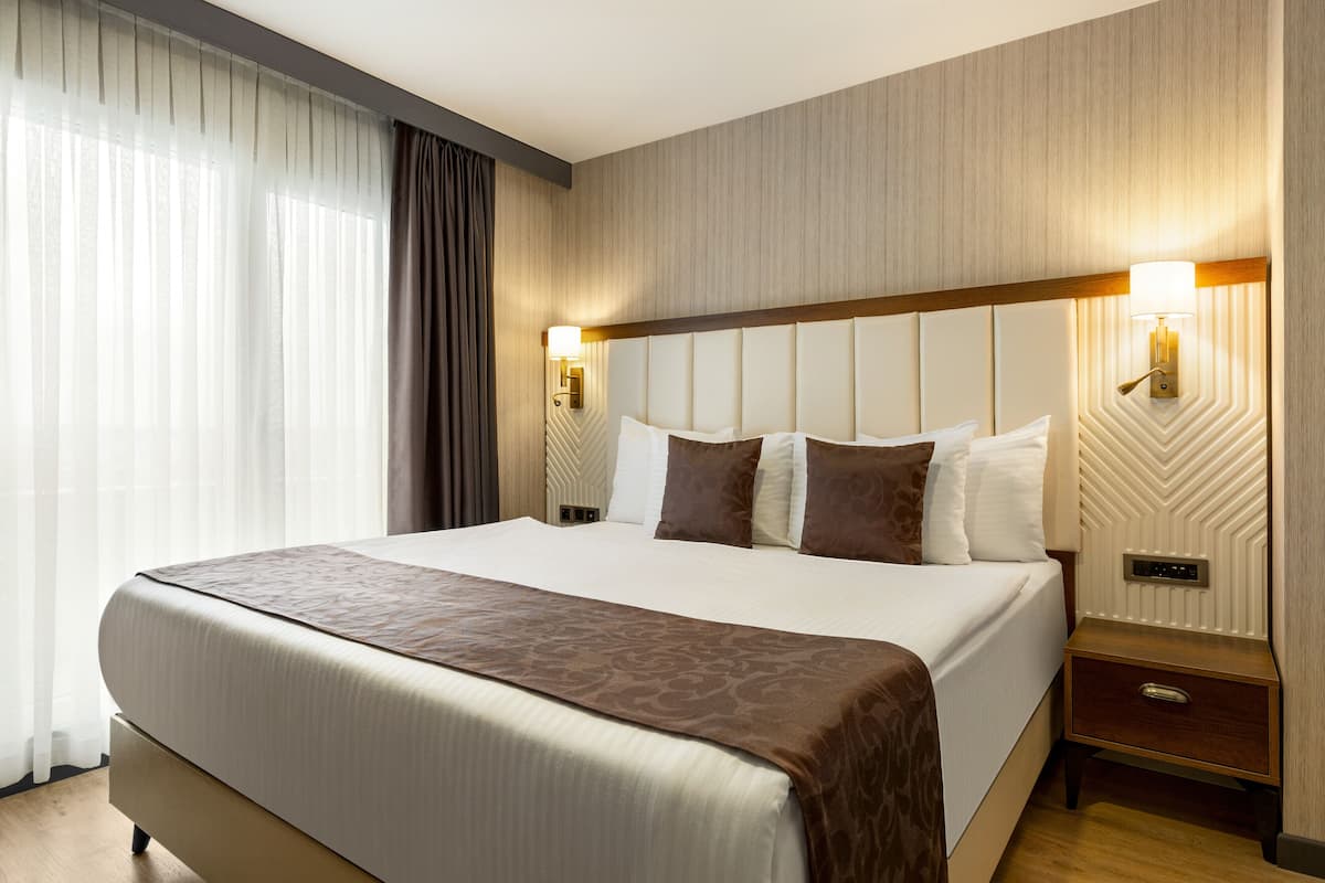 A hotel room with a large bed, two bedside tables, a nightstand, and a wall-mounted light fixture.