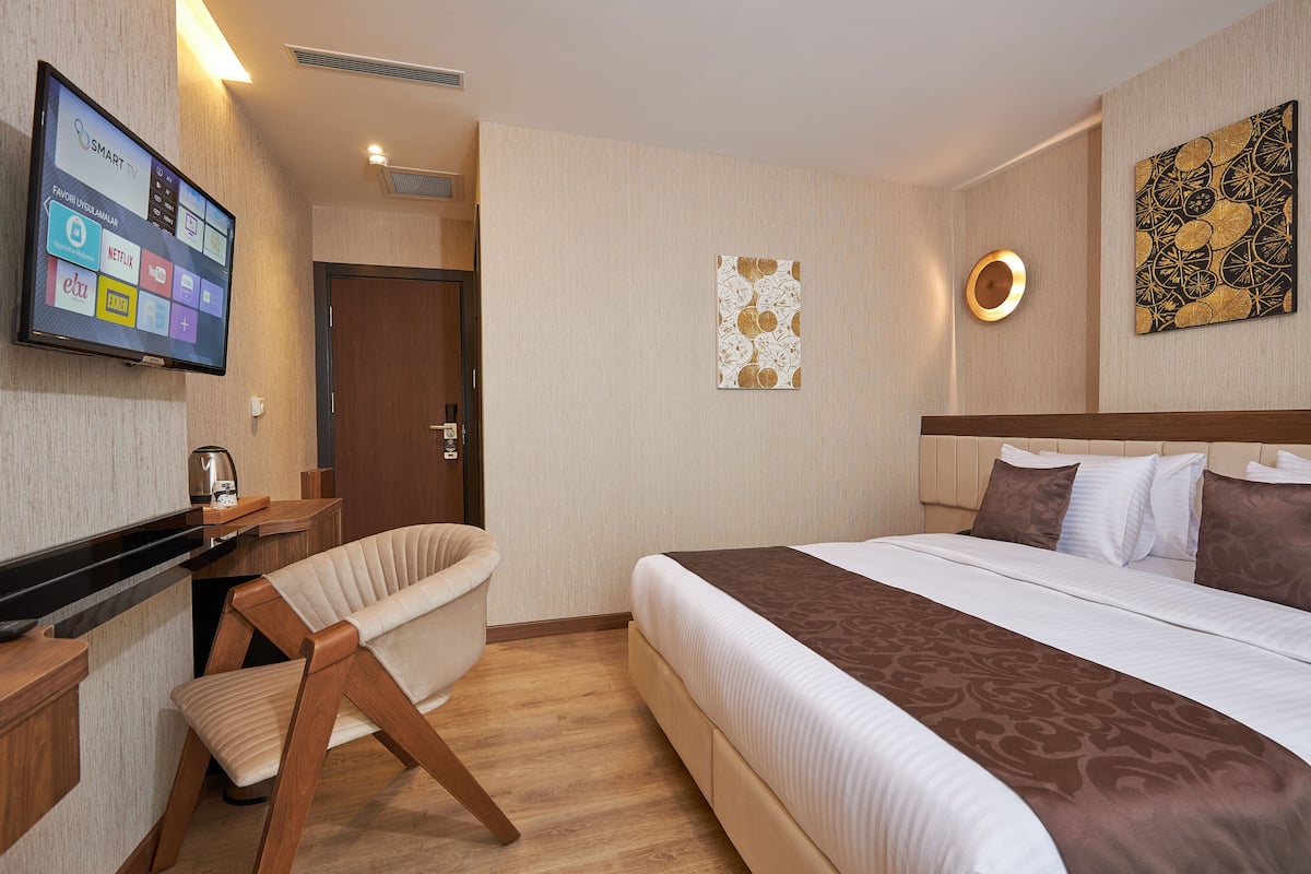 A hotel room with a bed, a desk, a chair, a TV displaying various apps, and a wall with a decorative piece.