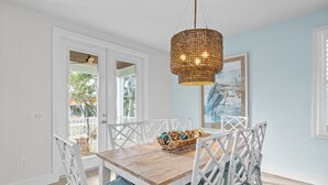 Un comedor con mesa de madera, sillas de mimbre blanco y una lámpara colgante tejida.