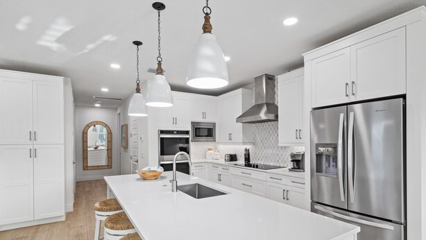 Una cocina moderna con armarios blancos, electrodomésticos de acero inoxidable y una isla central con taburetes.