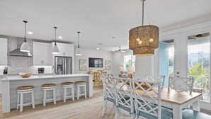 Una cocina moderna con armarios blancos, una isla central con taburetes, iluminación colgante y un ventanal con vistas.