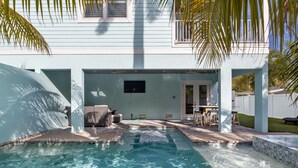 Una piscina con un jacuzzi, rodeada por un porche cubierto con mobiliario exterior.