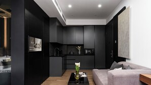 A modern living room with a sofa, a coffee table with flowers, a kitchen area with dark cabinets, and a large painting on the wall. - Stay Inn  on Buzand Str. 97 (Yerevan)