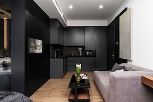 Een moderne woonkamer met een bank, een salontafel met bloemen, een keuken met donkere kasten en een groot schilderij aan de muur.