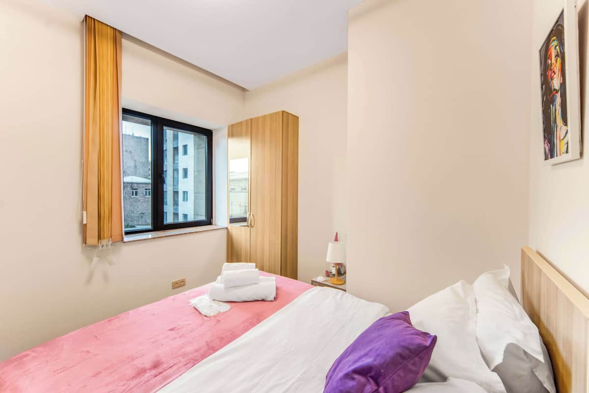 Een hotelkamer met een bed, een raam, een kledingkast en een schilderij aan de muur.