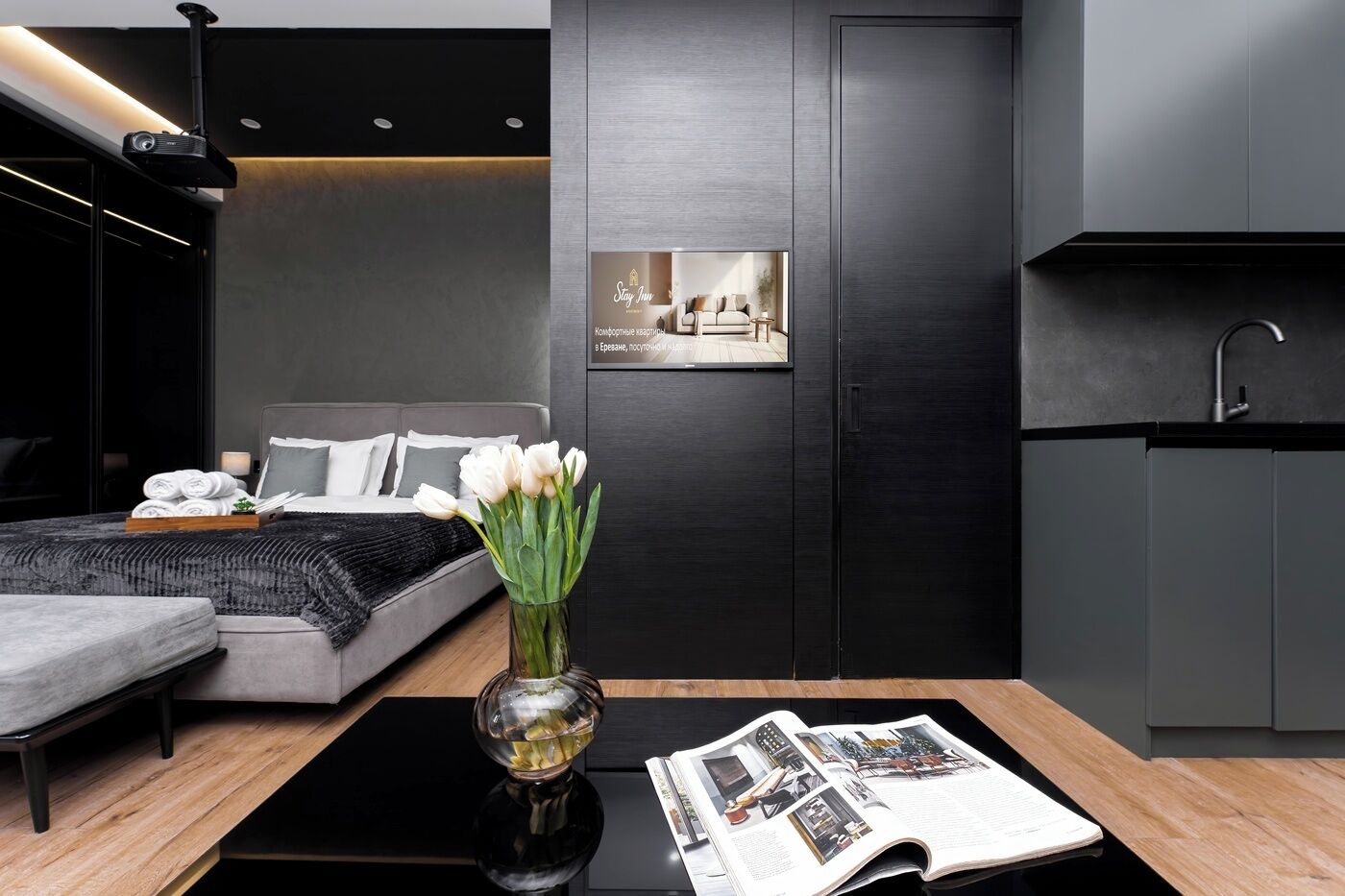 A modern hotel room with a bed, bedside table, and a view of a cityscape through a window.