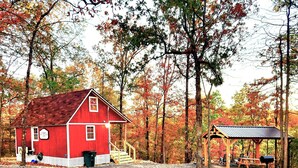 Eine rote Holzhütte mit Veranda und einem kleinen Nebengebäude in einem Waldgebiet.