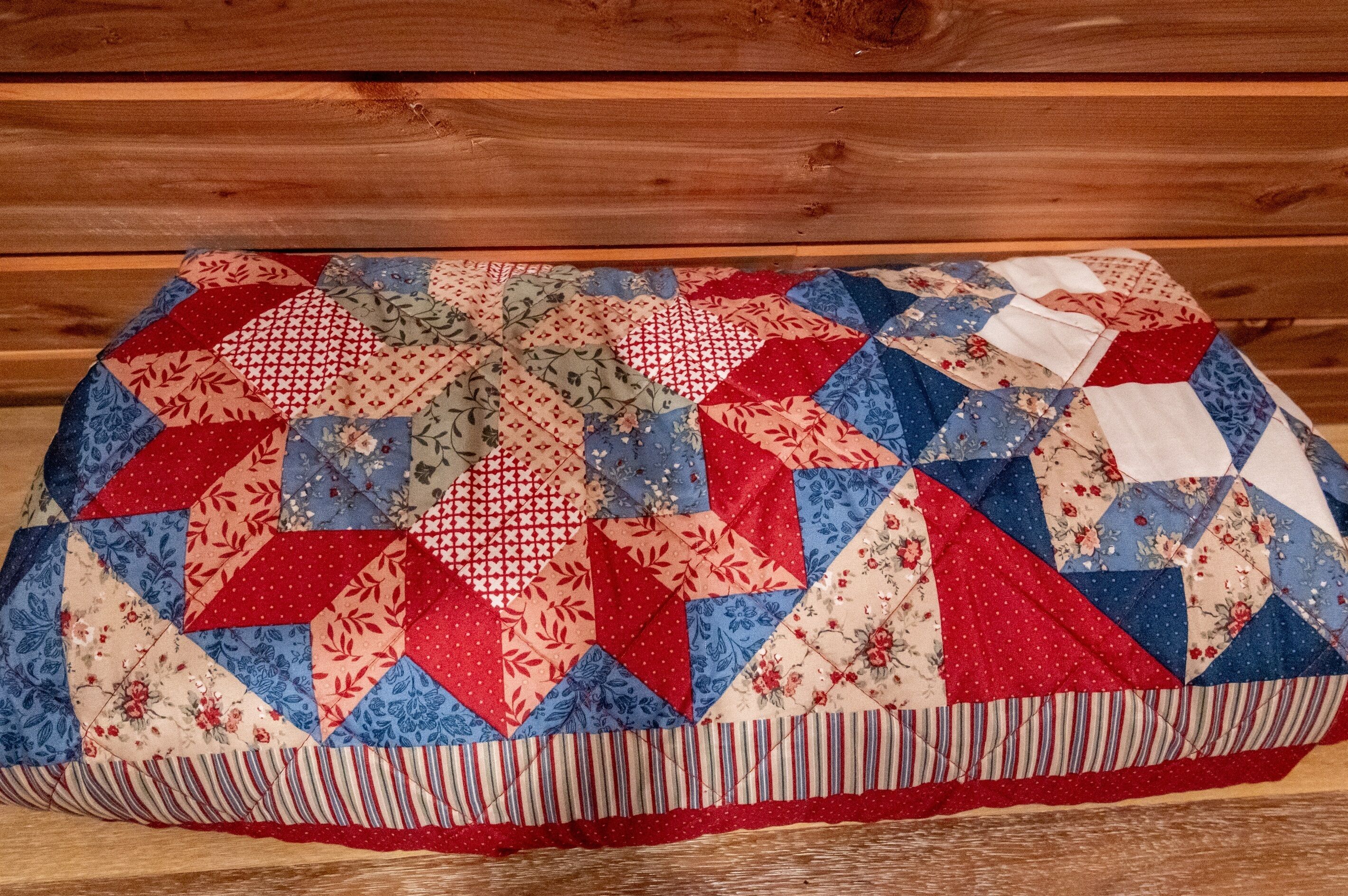 A quilted blanket with a geometric pattern, placed on a wooden bench.
