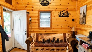 Ein Holzblockbau-Innenraum mit einer Couch, einem Kamin, einer Tür und einem Fenster.