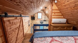 Ein gemütliches Schlafzimmer im Dachgeschoss mit Holzwänden, einem Bett mit gemustertem Überwurf, einem Deckenventilator und einer eingebauten Klimaanlage.