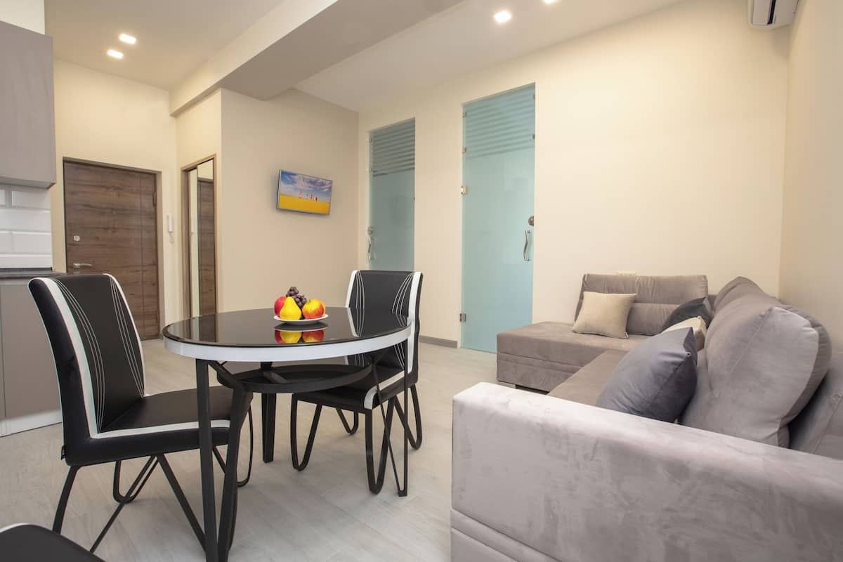 A modern living room with a round dining table, two black chairs, a grey sofa, and a blue door in the background.