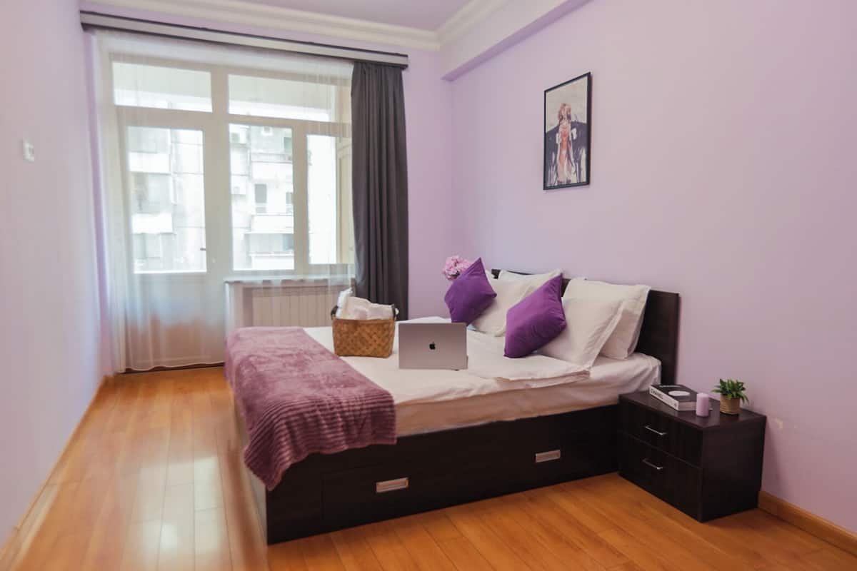 A bedroom with a bed, a laptop, a basket, and a nightstand.