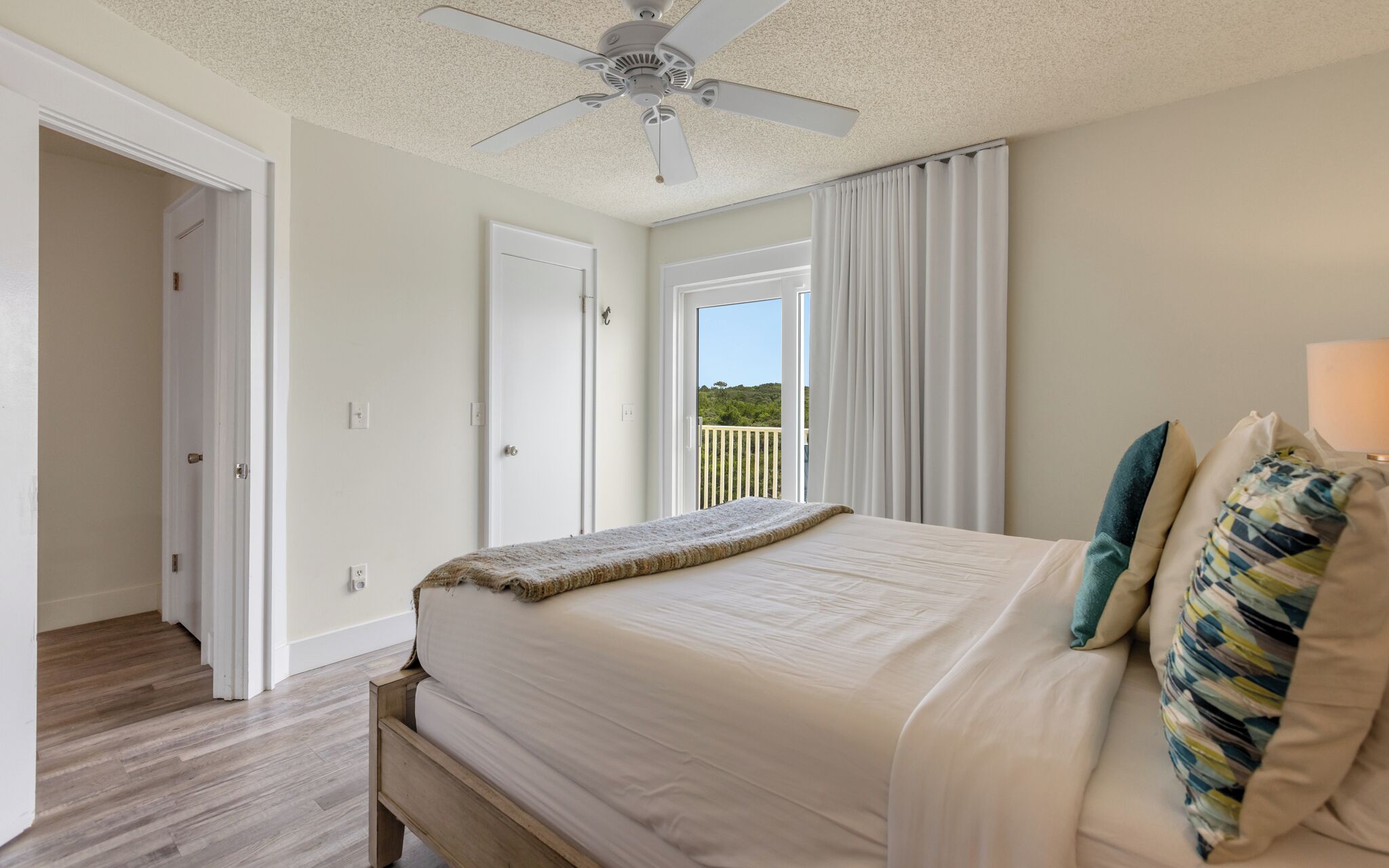 A bedroom with a bed, a ceiling fan, a window with curtains, and a view of greenery outside.