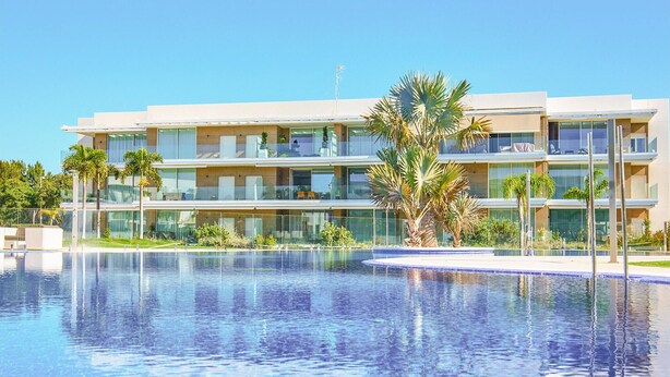 Ett modernt hotell med en stor pool, flera balkonger och palmer.