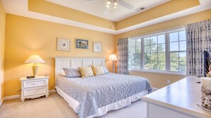 Un dormitorio con cama, mesitas de noche, una ventana con cortinas e imágenes enmarcadas en la pared.