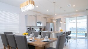 A modern kitchen with white cabinets, stainless steel appliances, and a dining area with a wooden table and grey upholstered chairs. - Stylish family friendly, 5 suites near Disney! (Davenport)