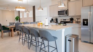 A modern kitchen with a central island, bar stools, stainless steel appliances, and pendant lighting. - Stylish family friendly, 5 suites near Disney! (Davenport)