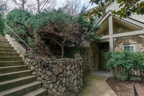 A stone staircase leading to a house with a stone wall and a small garden area.