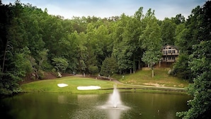 A golf course with a pond, a fountain, and a house in the background. - Stonecrest 162 at Rumbling Bald (Lake Lure)