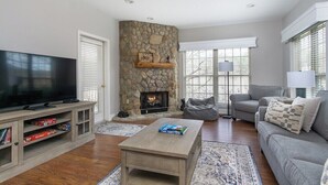 A living room with a stone fireplace, a flat-screen TV, a grey sofa, and a coffee table. - Stonecrest 162 at Rumbling Bald (Lake Lure)