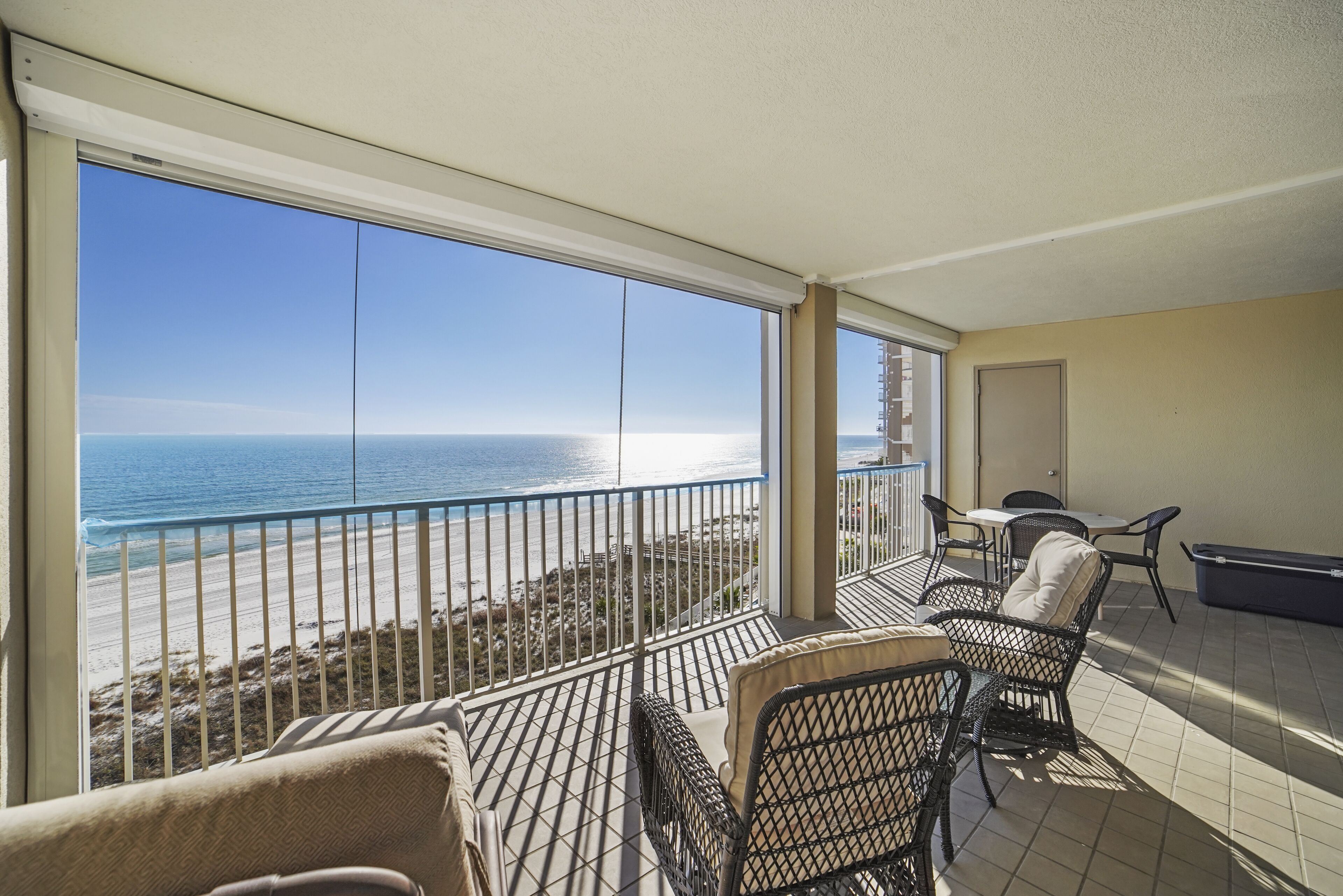 A balcony with a view of the beach, a table, and two chairs.
