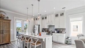 A modern kitchen with white cabinetry, a central island with bar stools, stainless steel appliances, and pendant lighting.