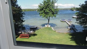 A view through a window of a lake with a grassy area, a tree, and a dock with boats.