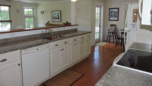 A kitchen with white cabinets, granite countertops, a dishwasher, and a dining area with a wooden table and chairs.