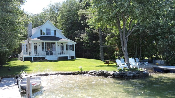 A white house with a porch and a small pond with chairs.