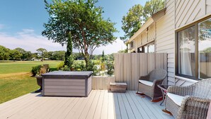 Eine Terrasse mit Gartenmöbeln, einem Whirlpool und Blick auf einen Golfplatz.