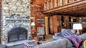 Interior acogedor de una cabaña de troncos con chimenea de piedra, muebles de madera y un techo alto.