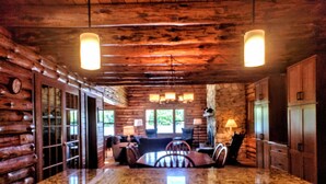 Interior de una cabaña de troncos con cocina que incluye encimeras de granito, una mesa de comedor con sillas y una chimenea.
