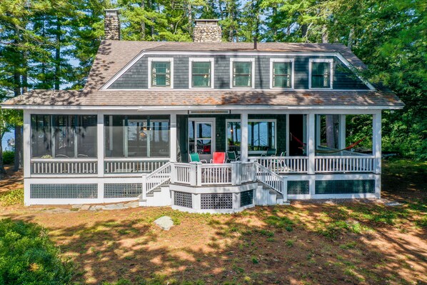 A two-story house with a covered porch, large windows, and a stone chimney.