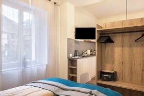 Une chambre avec un lit, une télévision, un coin cuisine et une armoire en bois.