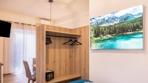 A bedroom with a wooden wardrobe, a bed with a blue and grey blanket, a desk with a chair, and a painting of a mountain landscape. - Apartment "Annabel" with Mountain View, French Balcony & Wi-Fi (Bolzano)