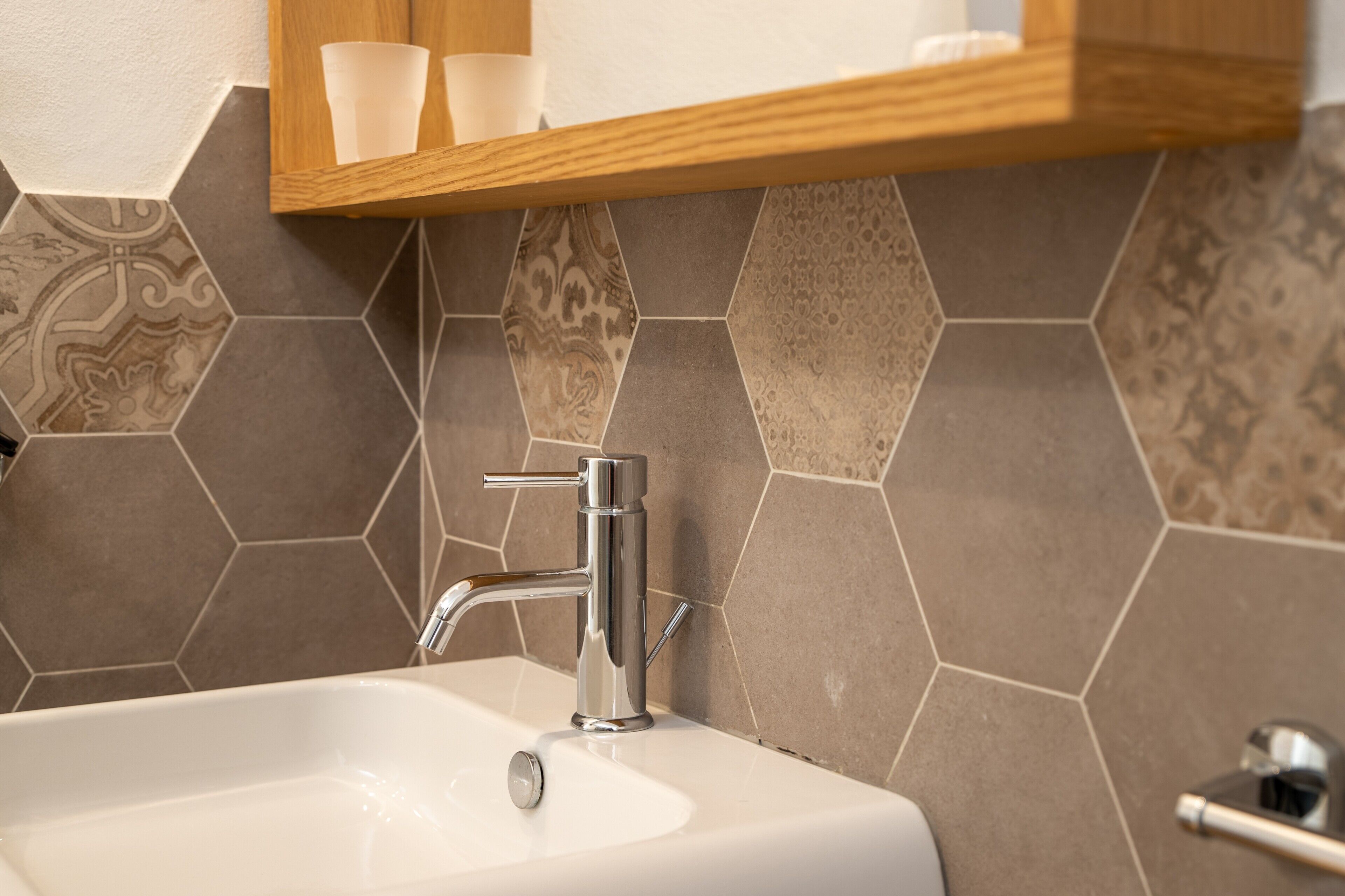 Un bagno con un lavandino bianco, un rubinetto cromato e uno scaffale in legno sopra.
