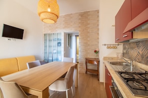 Uma cozinha moderna com uma mesa de madeira, cadeiras, uma TV fixada na parede e um armário vermelho.