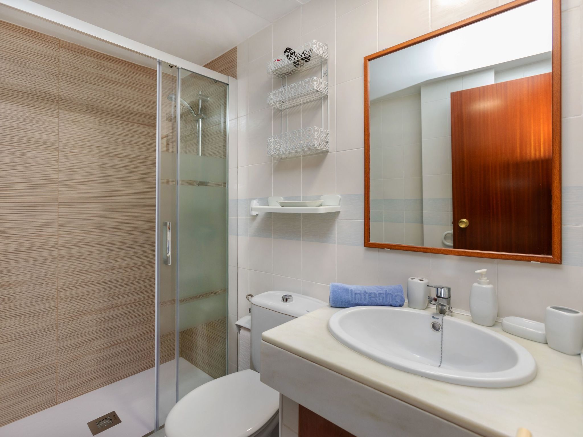 Ein modernes Badezimmer mit Duschkabine aus Glas, einer weißen Toilette, einem Waschbecken mit Spiegel und einer Holztür.