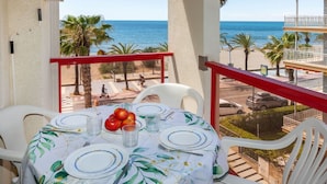 A balcony with a table set for two, overlooking a beach and palm trees. - Apartment Ancora by Interhome (Salou)