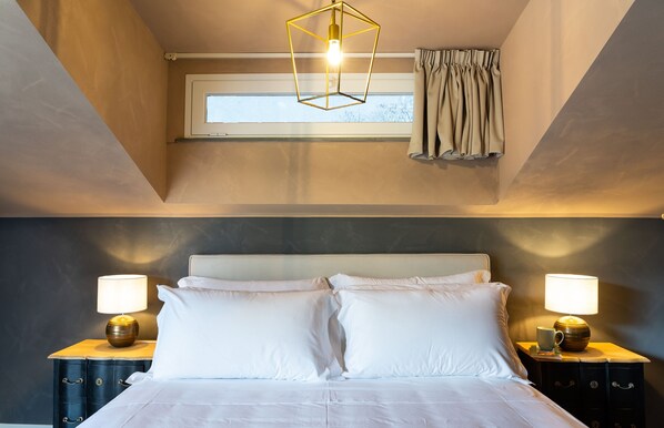 A bedroom with a bed, two bedside tables with lamps, a window with curtains, and a geometric light fixture.