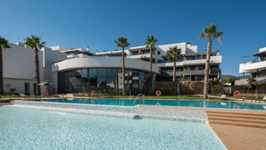 Un hotel moderno con una grande piscina, palme e un cielo azzurro intenso.