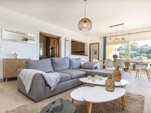 Uma sala de estar moderna com um sofá seccional cinza, uma mesa de centro redonda e uma área de jantar com cadeiras e uma mesa.