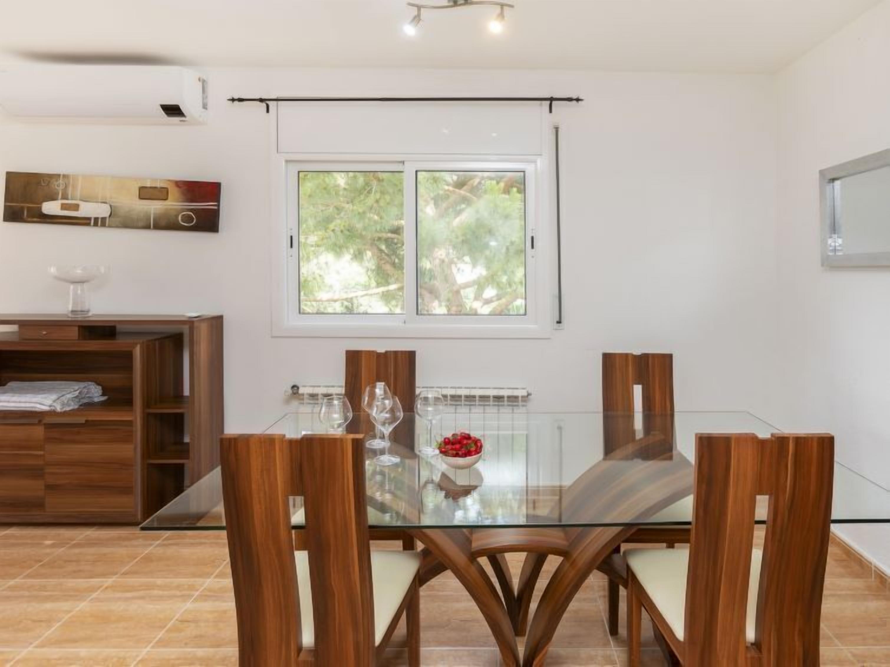 Comedor con una mesa de vidrio, sillas de madera y vista a la vegetación por una ventana.