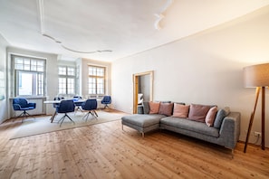 A modern living room with a grey sectional sofa, a dining area with a table and chairs, and large windows allowing natural light.