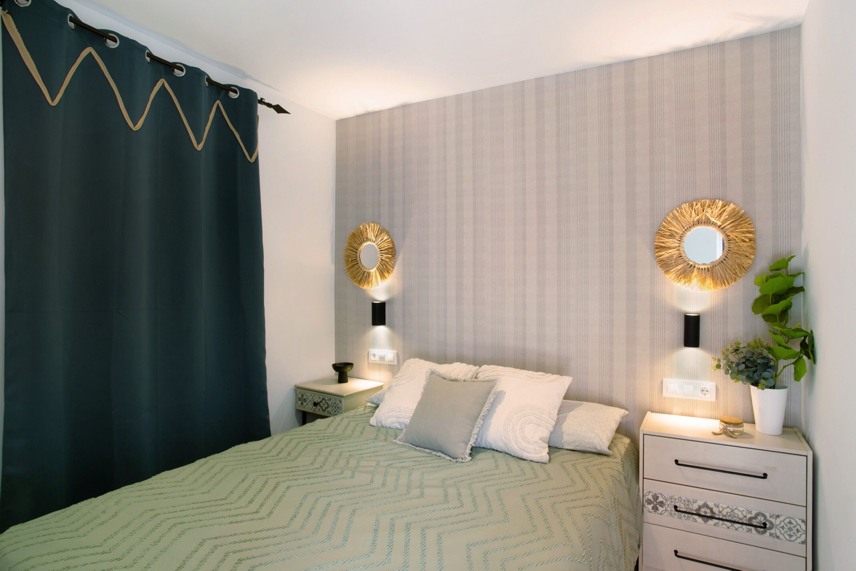 Een slaapkamer met een bed, twee nachtkastjes, een spiegel en een potplant.