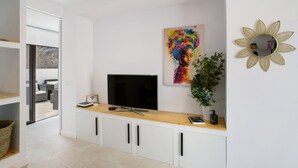 A modern living room with a flat-screen TV, a colorful abstract painting, a decorative sun-shaped mirror, and a potted plant. - Vacation 'Dreaming Penthouse Mogan' with Mountain View, Wi-Fi and Air Conditioning (Mogán)