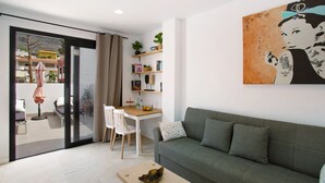 A modern living room with a sofa, a dining table with chairs, a glass door leading to an outdoor area, and a wall-mounted shelf with books and plants. - Vacation 'Dreaming Penthouse Mogan' with Mountain View, Wi-Fi and Air Conditioning (Mogán)